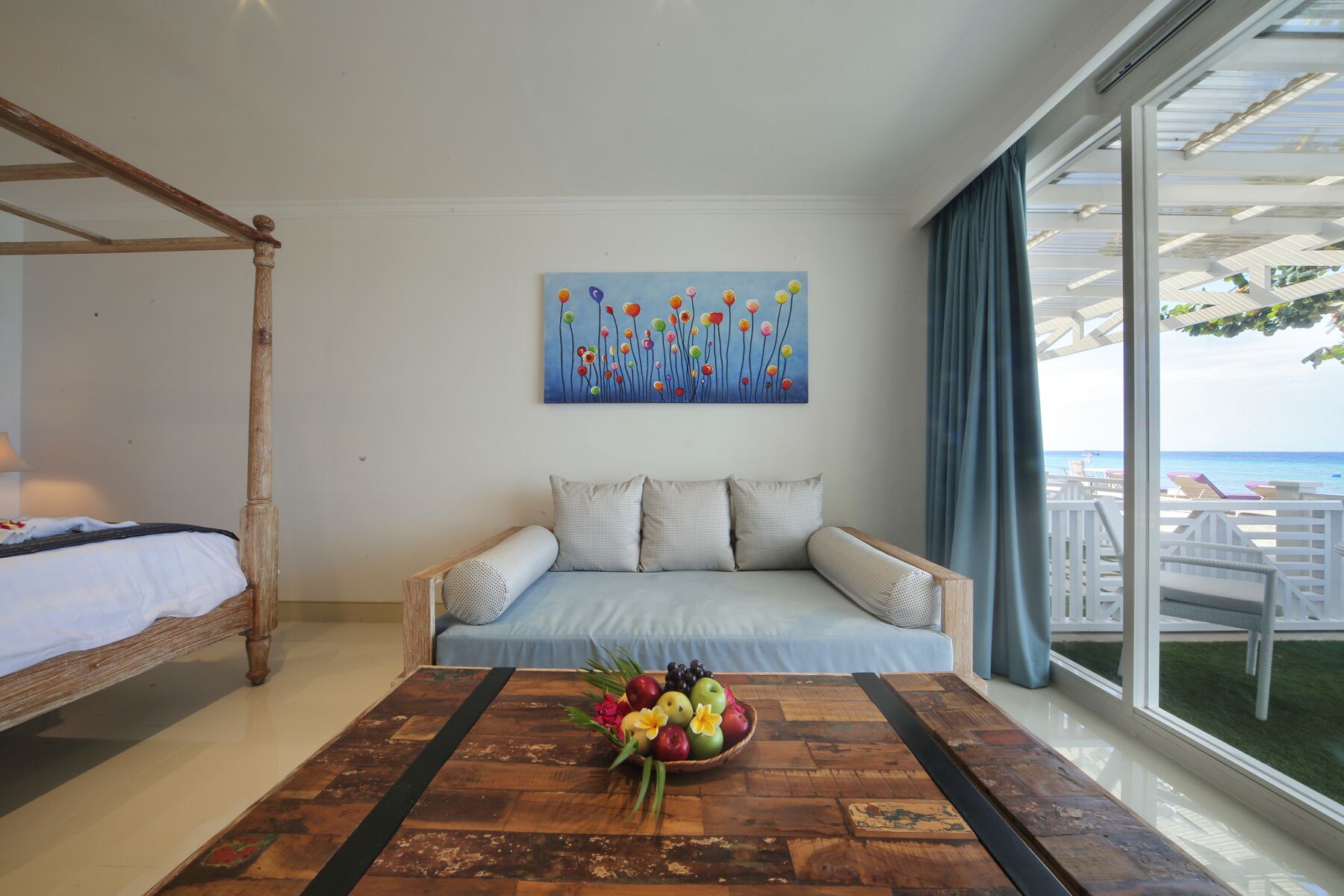 Un dormitorio con una cama con dosel de madera, un sofá con cojines estampados, un cuadro de flores y un frutero sobre una mesa de madera.
