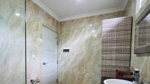Un bagno con parete in marmo, cabina doccia in vetro, water bianco, lavabo con piano in nero e ripiano in vimini.