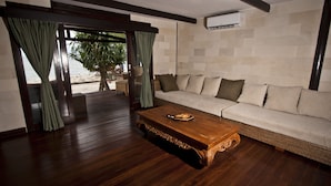 Un soggiorno con un tavolino in legno, un divano color beige e vista sulla spiaggia tramite una porta in vetro.
