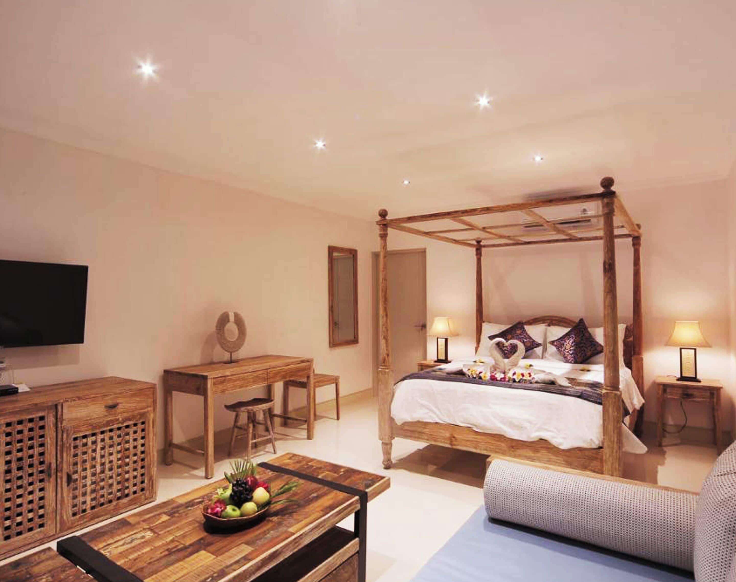 Een slaapkamer met een hemelbed, een houten bureau, een televisie en een fruitschaal op de tafel.