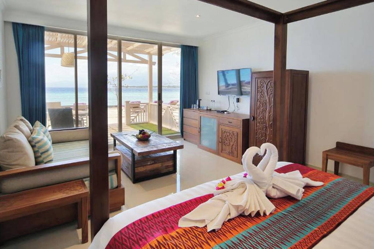 A hotel room with a bed, a desk, a TV, and a view of the ocean.