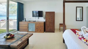 Una camera d'hotel con un'ampia finestra, un letto decorato con motivi floreali, un comò in legno, un televisore a schermo piatto e un tavolo da pranzo con frutta.