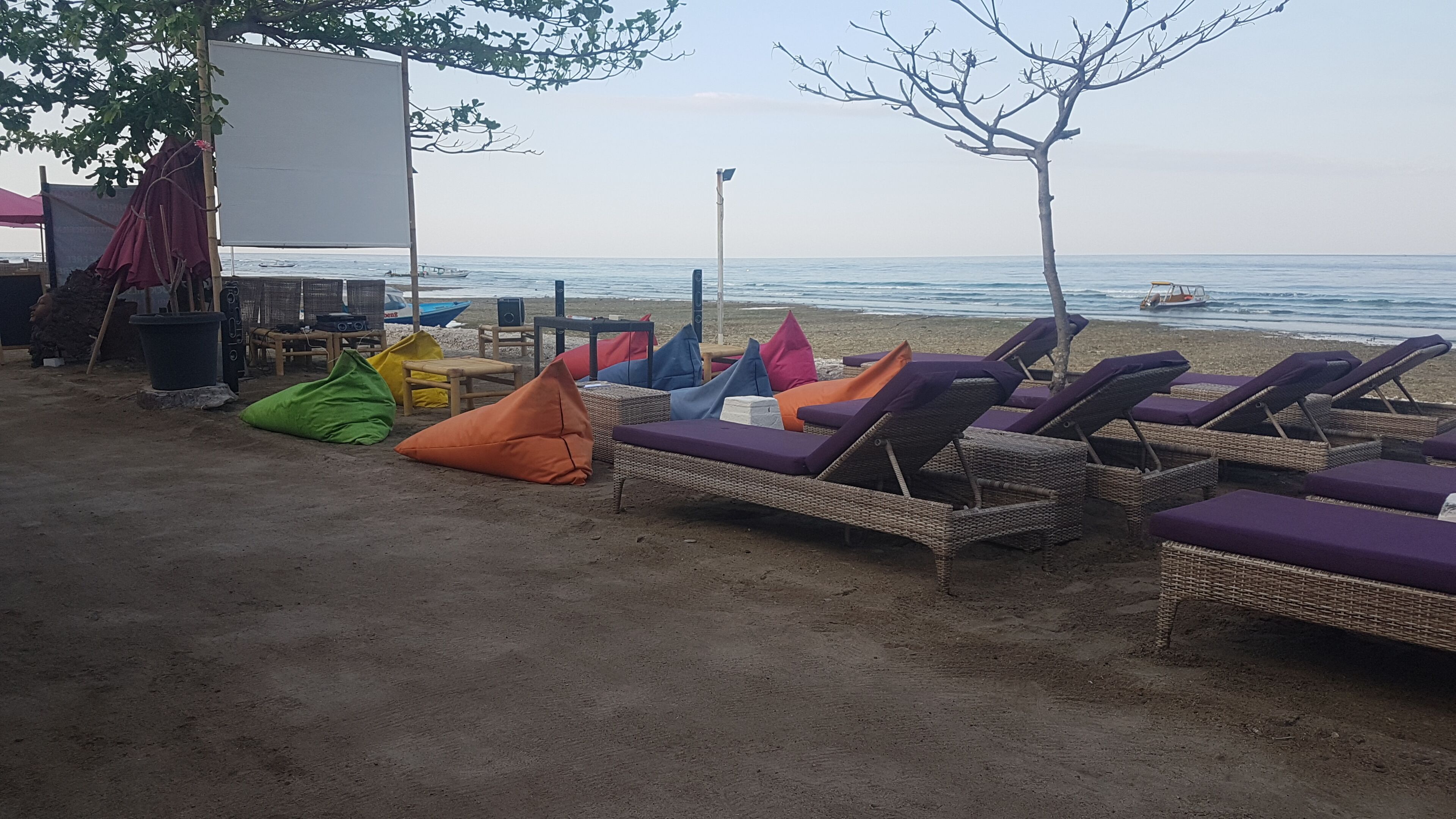 Un área de descanso frente a la playa con sillones de mimbre y cojines de colores, una pizarra y un sistema de sonido.