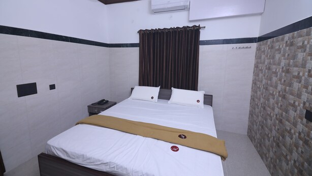 A hotel room with a bed, a nightstand, an air conditioning unit, and a patterned wall. - GM Residency (Chennai)