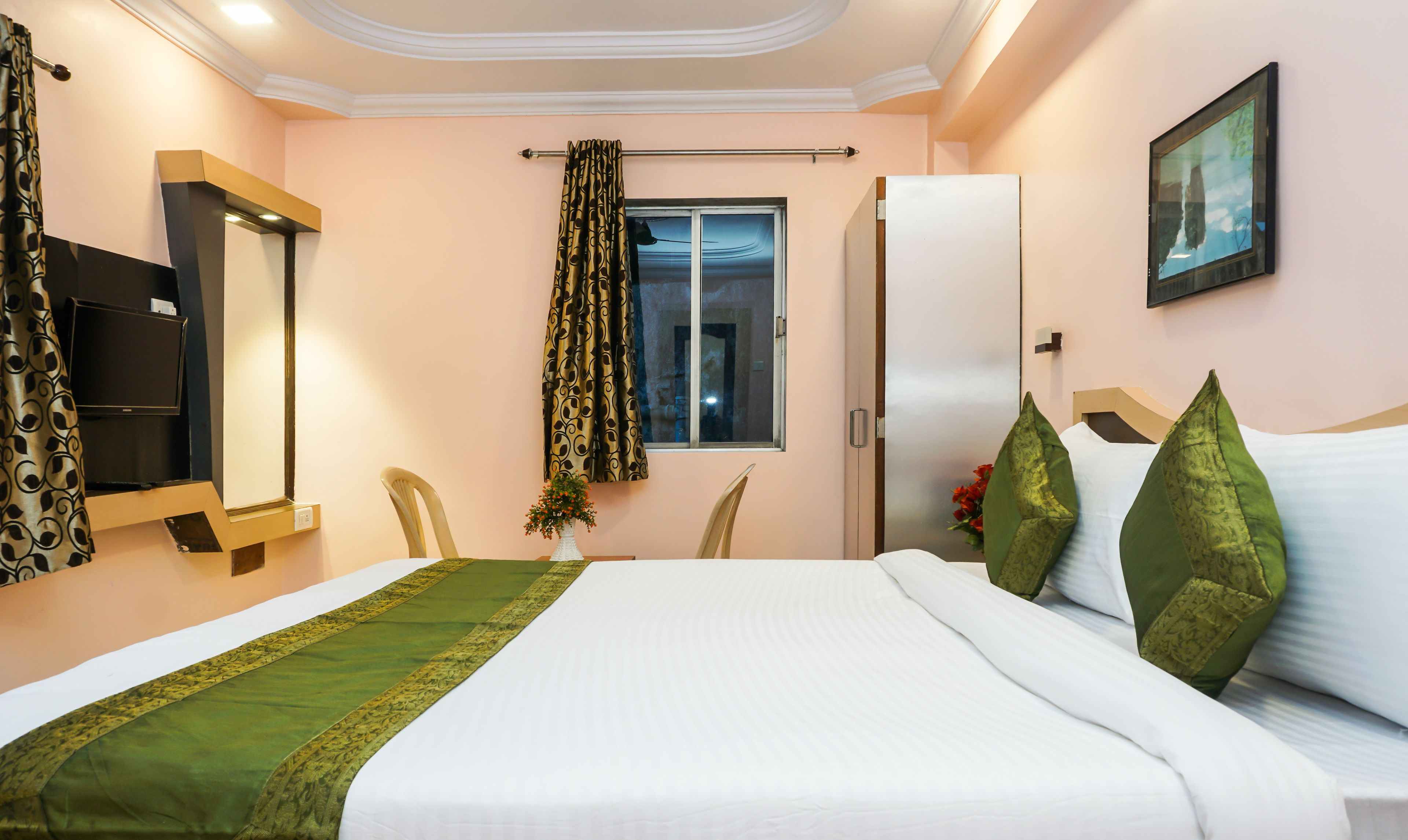 A hotel room with a bed, a TV, a window with curtains, a door, and a painting on the wall.