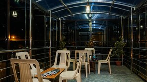 A covered outdoor seating area with plastic chairs and tables, potted plants, and a view of the city at night. - Treebo Hillway Inn Main Market (Mahabaleshwar)