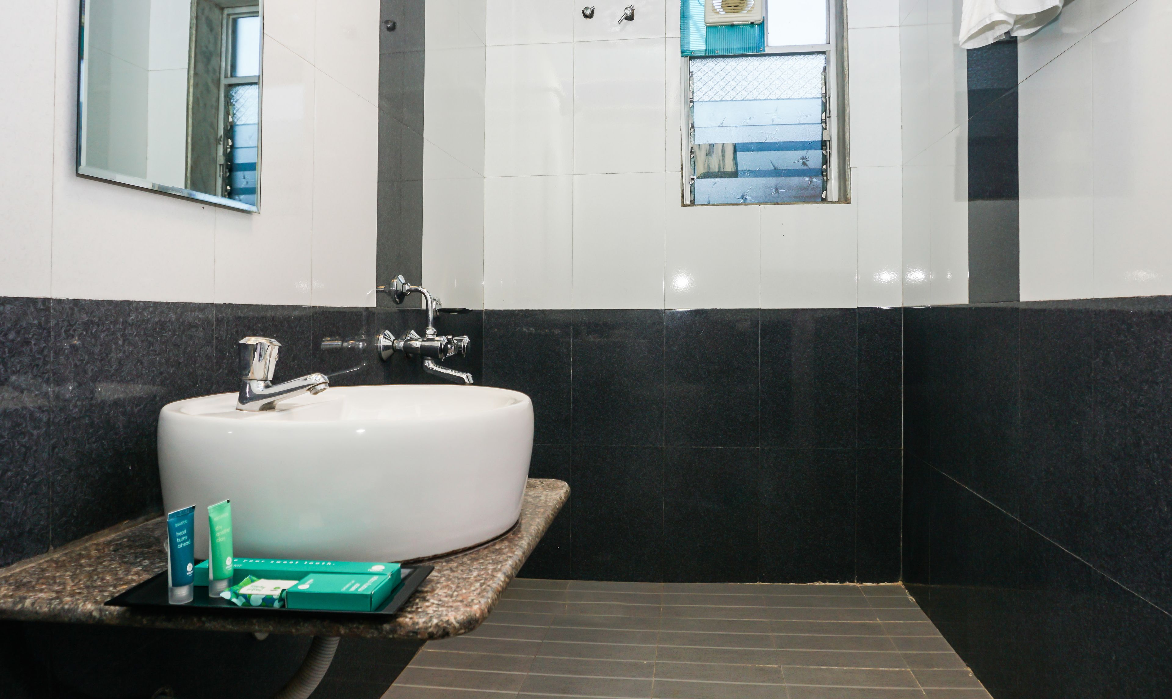 Une salle de bain avec un lavabo blanc, un miroir et une fenêtre donnant sur l’extérieur.