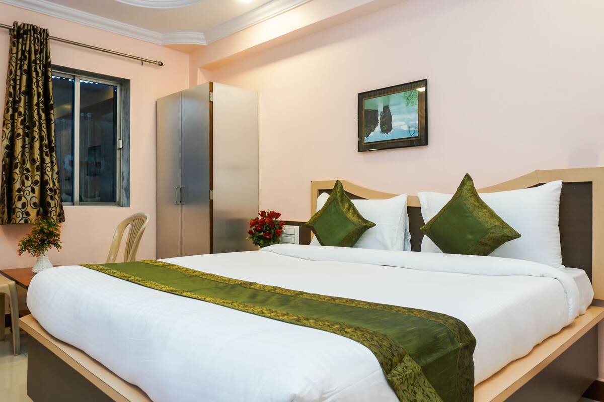 A hotel room with a bed, a chair, a wardrobe, a window with curtains, and a framed picture on the wall.
