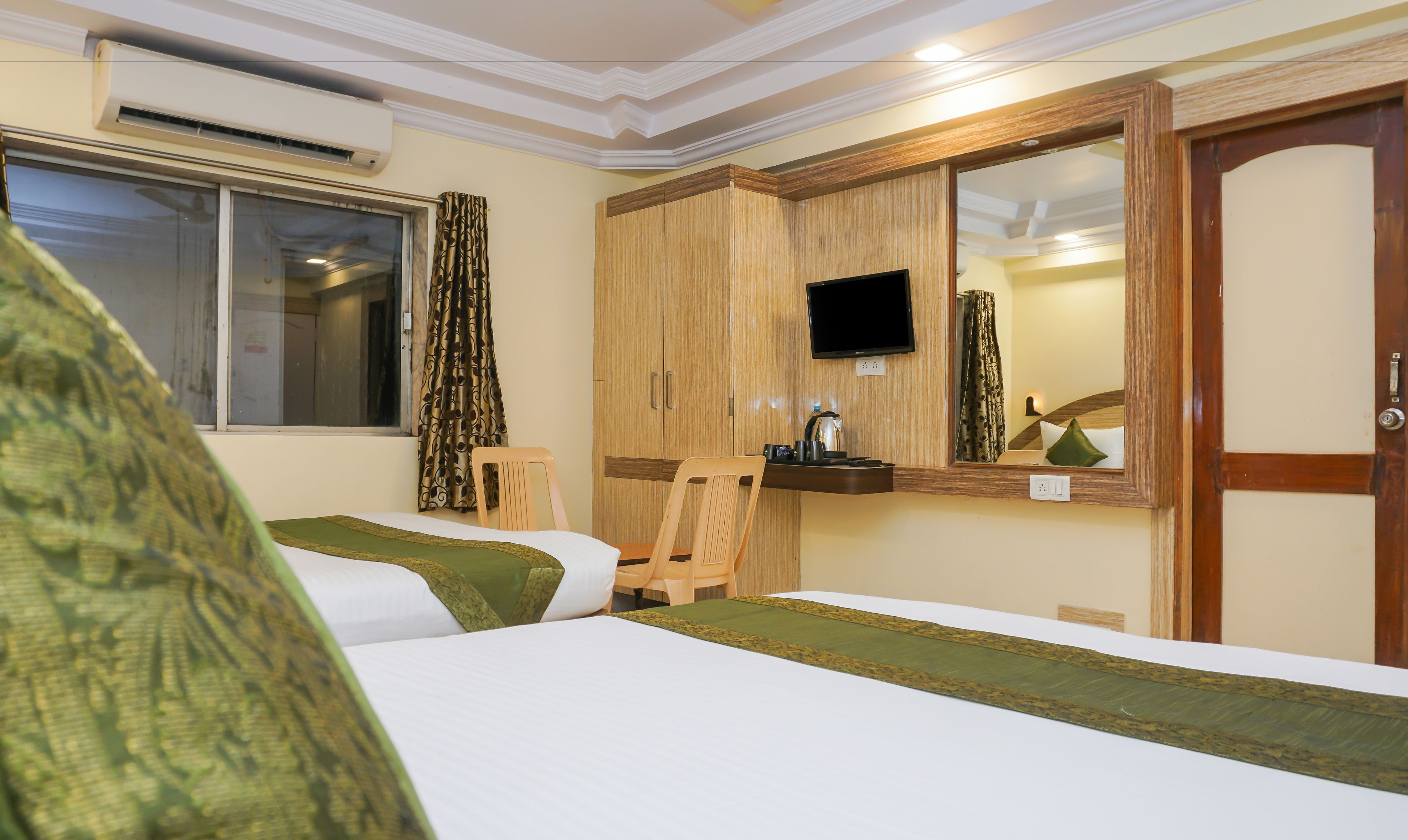 Une chambre d’hôtel avec deux lits, une armoire en bois, une télévision et un miroir.