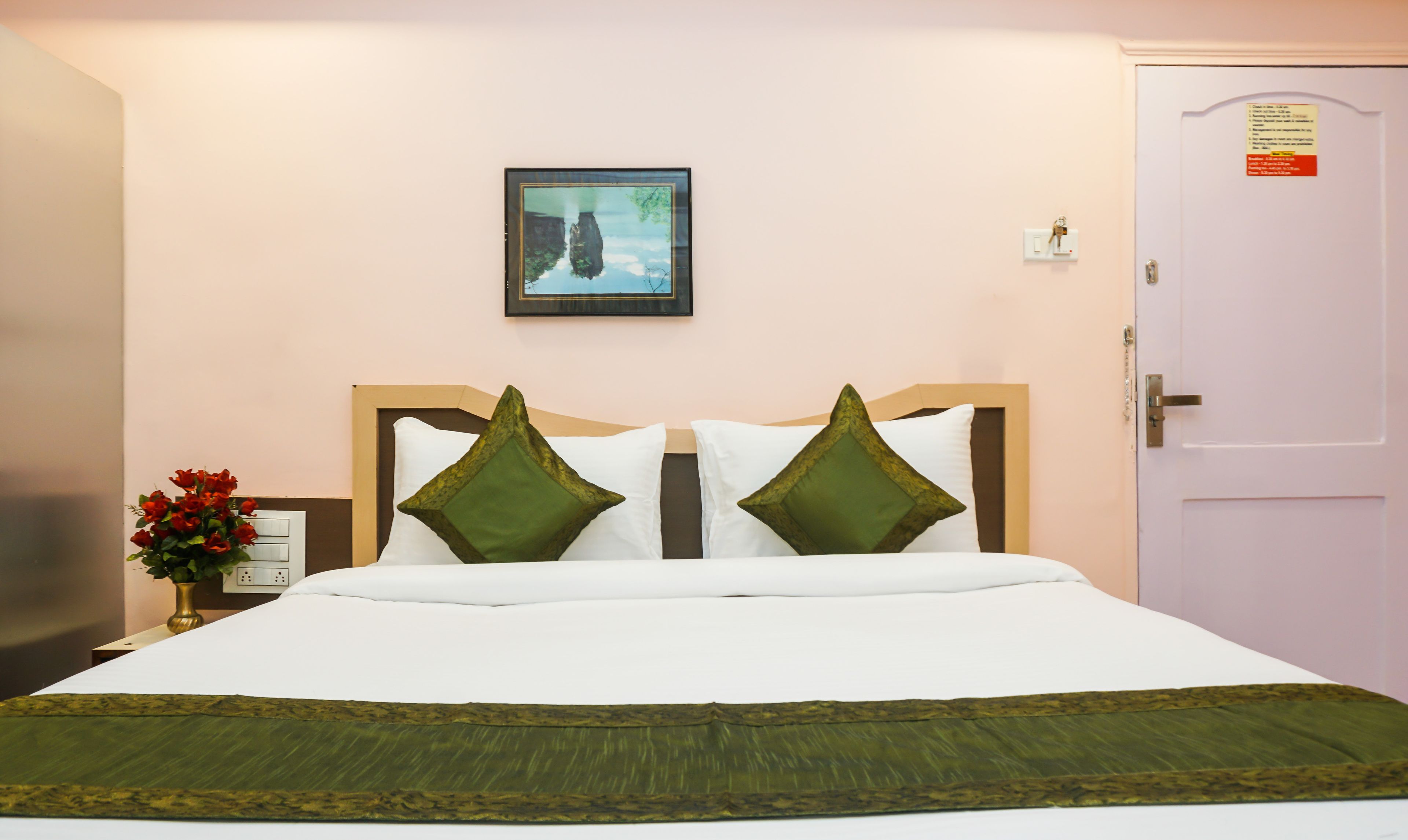 A neatly made bed with white and green bedding, a framed picture on the wall, and a door with a sign.