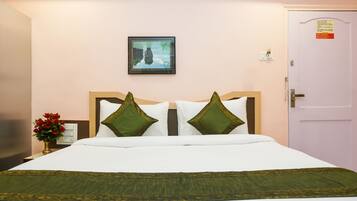 A neatly made bed with white and green bedding, a framed picture on the wall, and a door with a sign.