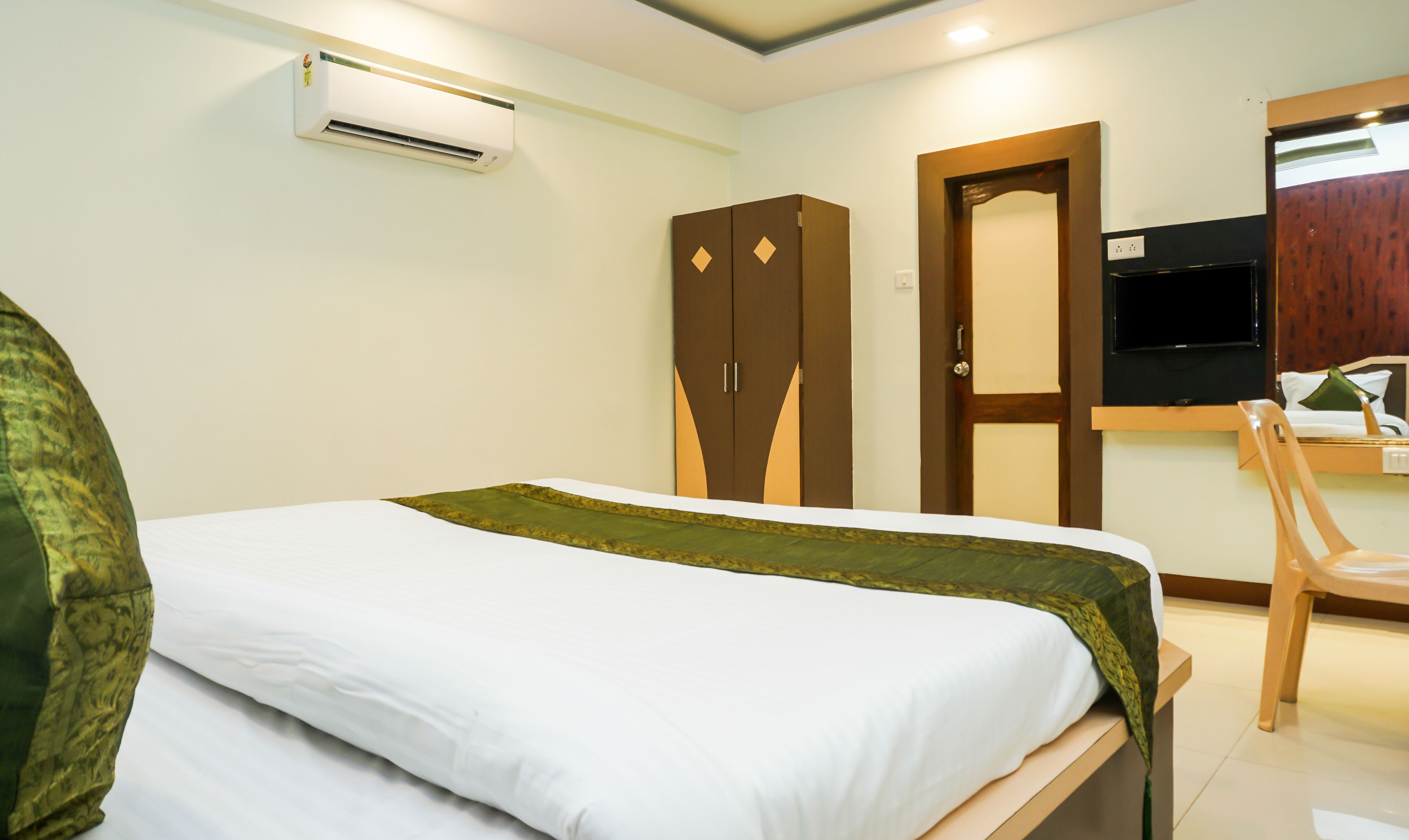 A hotel room with a bed, a desk, a chair, a wardrobe, and a television.