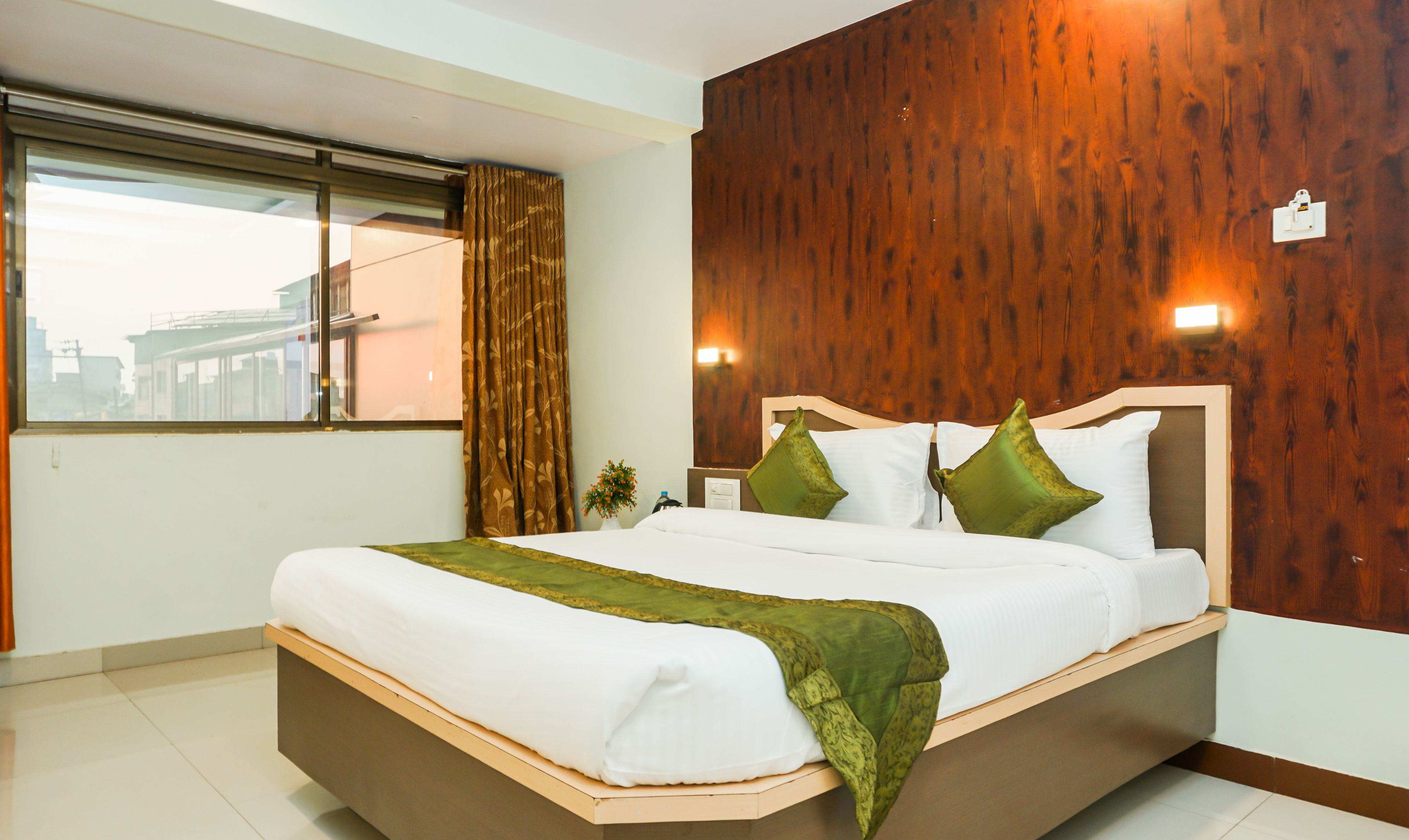 A neatly made bed with white and green bedding, a wooden headboard, and a window with curtains.