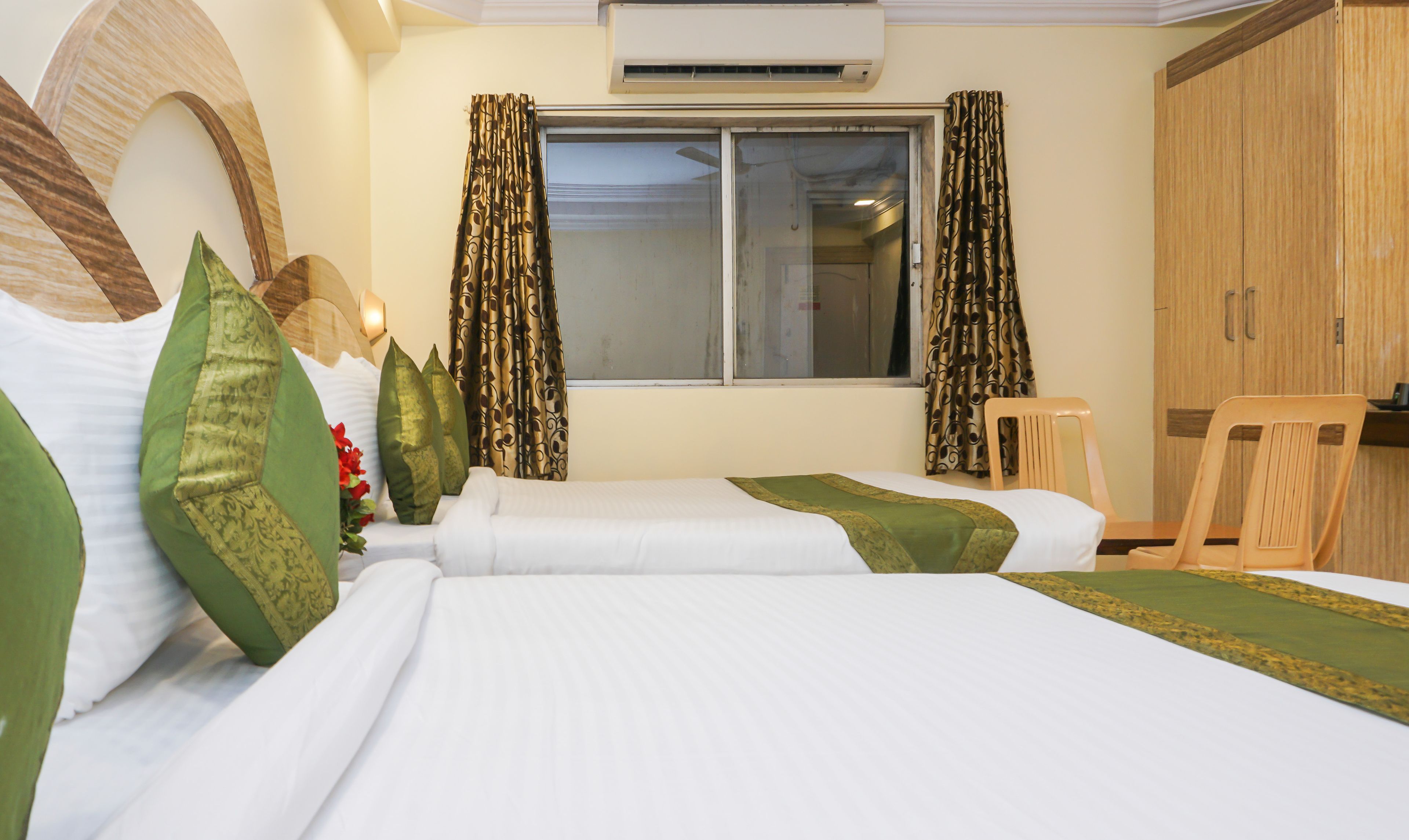 A hotel room with a bed, two pillows, a chair, a window with curtains, and a wardrobe.