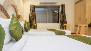 A hotel room with a bed, two pillows, a chair, a window with curtains, and a wardrobe.
