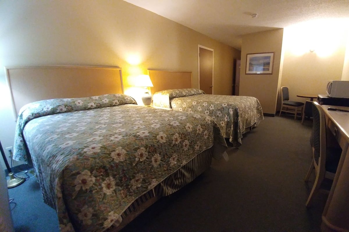 A hotel room with two beds, a desk, a chair, a computer, and a lamp.