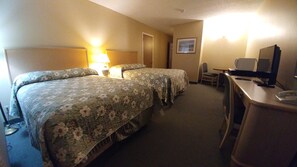 A hotel room with two beds, a desk, a chair, a computer, and a lamp.