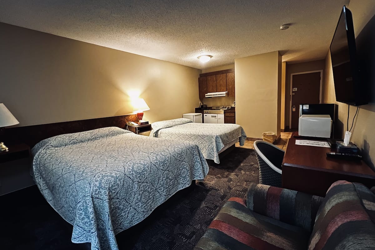A hotel room with two beds, a desk with a chair, a television, and a kitchenette.