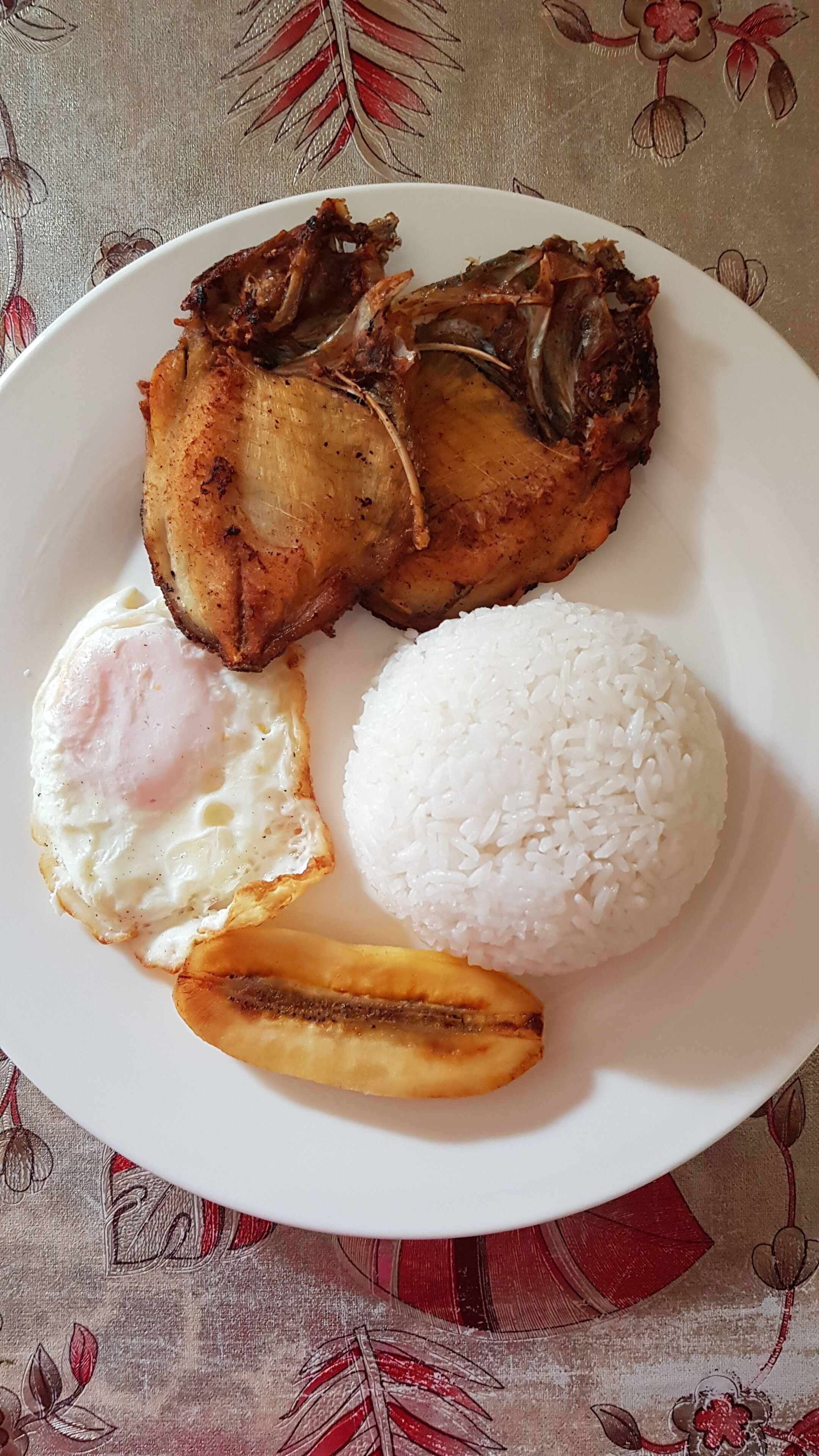 A plate with fried fish, a fried egg, white rice, and fried plantains.