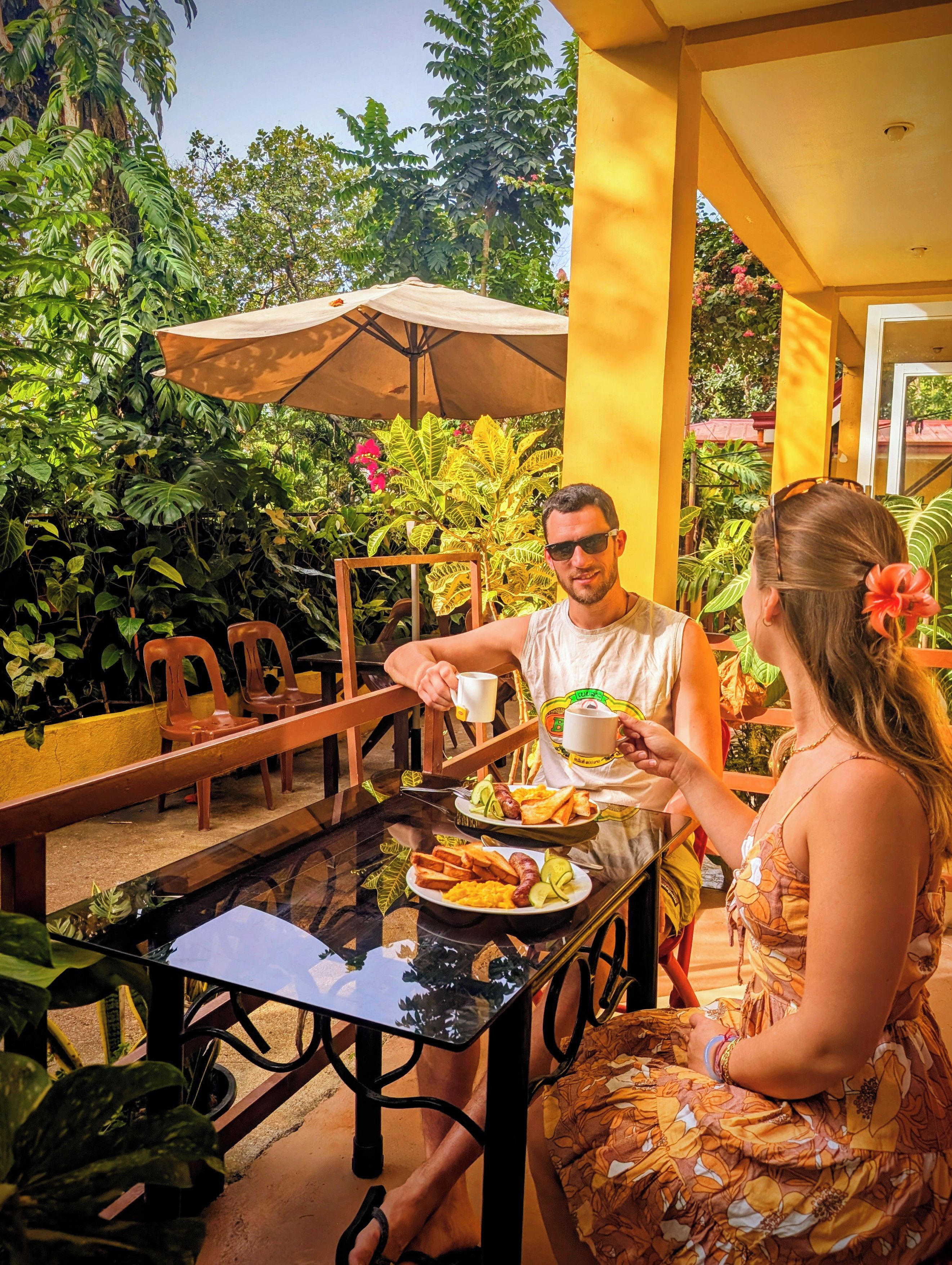 A dining table with chairs, a person holding a cup, and another person with a plate of food.