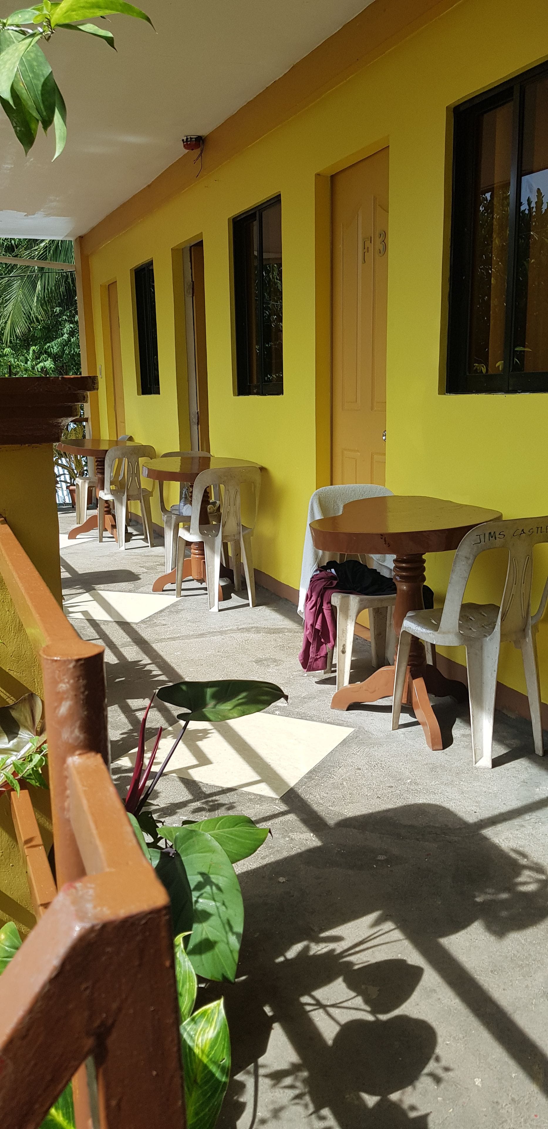 A covered outdoor seating area with tables and chairs, a yellow wall, and a door marked with the number 3.