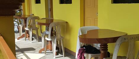 A covered outdoor seating area with tables and chairs, a yellow wall, and a door marked with the number 3.