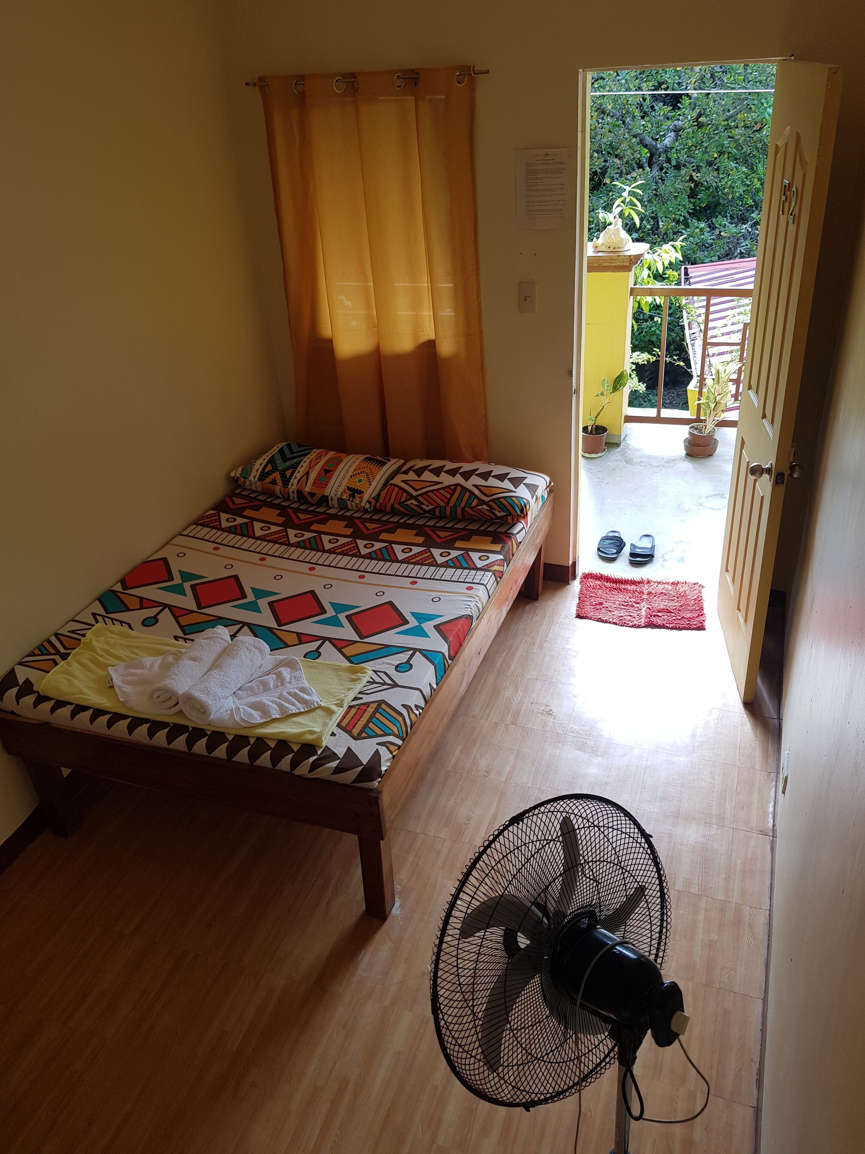 A room with a bed, a fan, and a view of the outside.