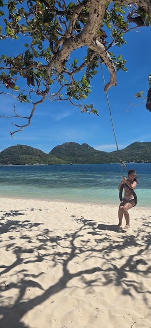 A beach scene with clear water, a tree, and a person. - Jim's Castle Inn (Coron)
