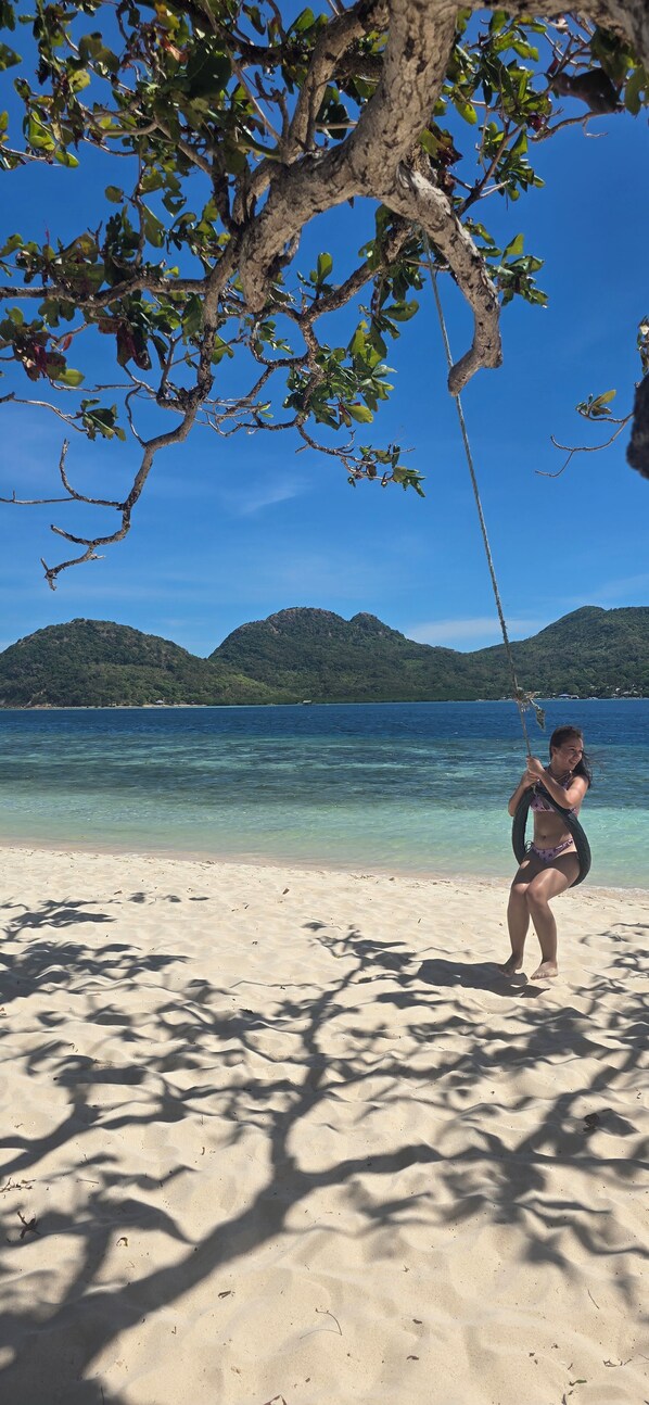 Escena de playa con agua cristalina, un árbol y una persona.