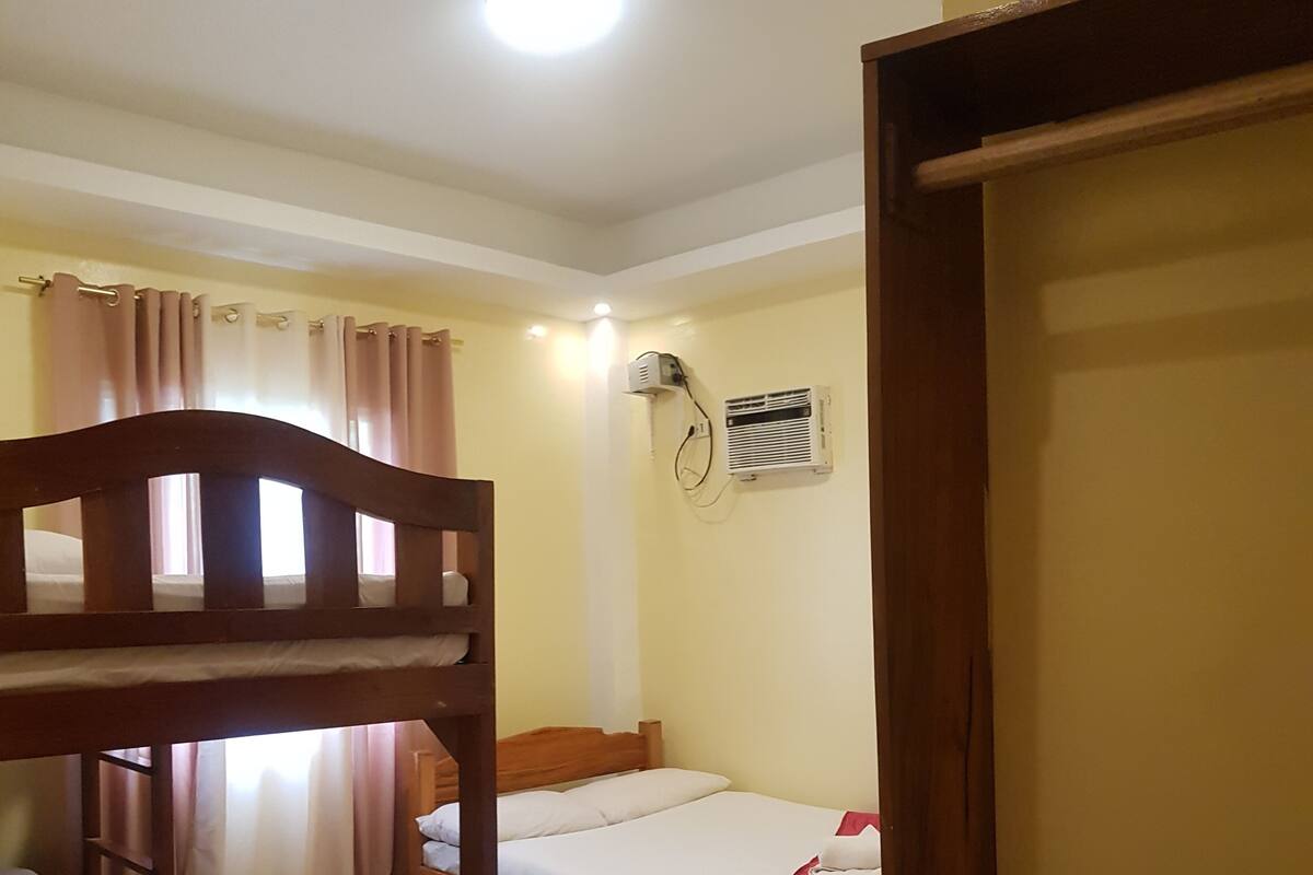 A room with two bunk beds, a single bed, a wall-mounted air conditioner, and a red rug.