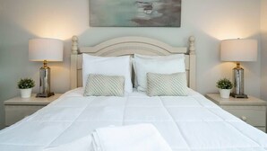 Una cama bien hecha con sábanas blancas, dos lámparas de noche y un cuadro sobre la cabecera.