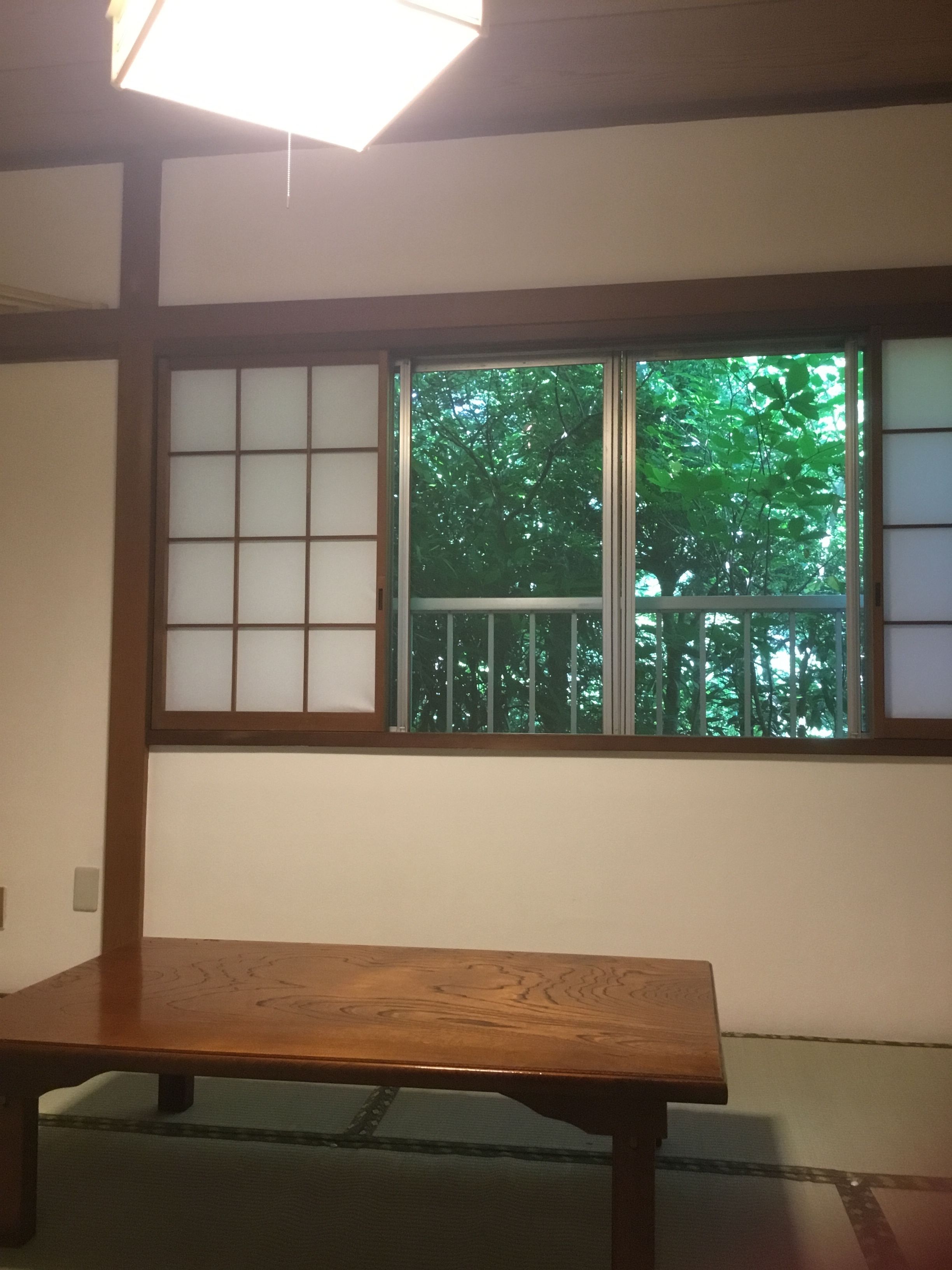 A traditional Japanese room with tatami flooring, a wooden table, and a shoji screen window overlooking a green tree.