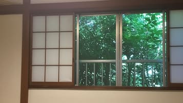 A traditional Japanese room with tatami flooring, a wooden table, and a shoji screen window overlooking a green tree.