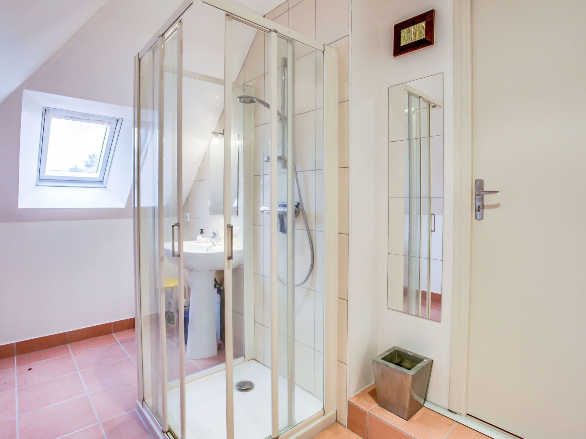 A modern bathroom with a glass-enclosed shower, a sink, and a small trash bin.