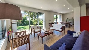 A spacious living room with a large window, a sofa, a coffee table, and a dining area. - Wonderful private villa for 8 people with WIFI, TV, terrace and pets allowed (Saint-philibert)