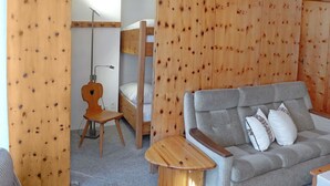 Une pièce chaleureuse avec un lit superposé, une chaise en bois, un canapé gris agrémenté de coussins et une petite table en bois.