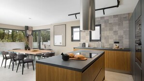 Une cuisine moderne dotée d’un îlot central, de meubles en bois et d’une grande fenêtre donnant sur un espace verdoyant.