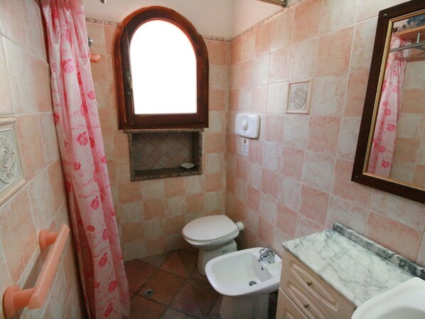 Un baño con inodoro, bidé, lavabo, tocador y una ventana sobre el inodoro.