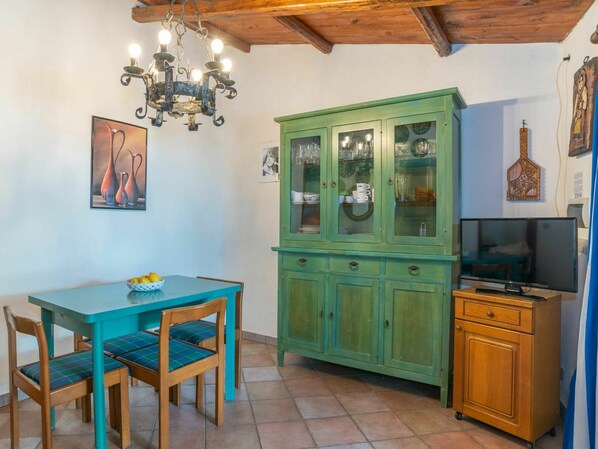 Un comedor con una mesa y sillas azul verdoso, un aparador verde con puertas de vidrio, una araña y un televisor sobre un mueble de madera.