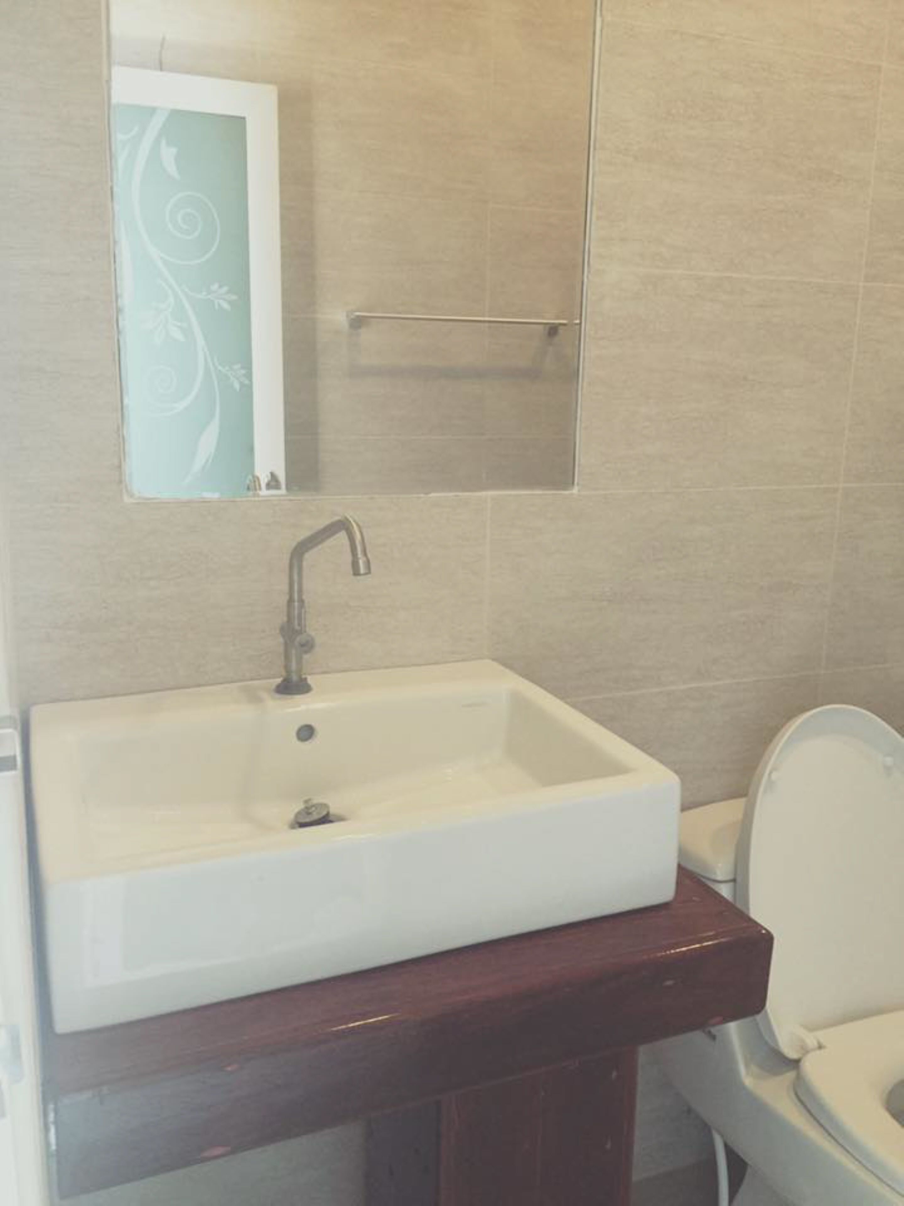 A bathroom with a white sink, a wooden vanity, a mirror, and a toilet.