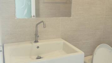 A bathroom with a white sink, a wooden vanity, a mirror, and a toilet.