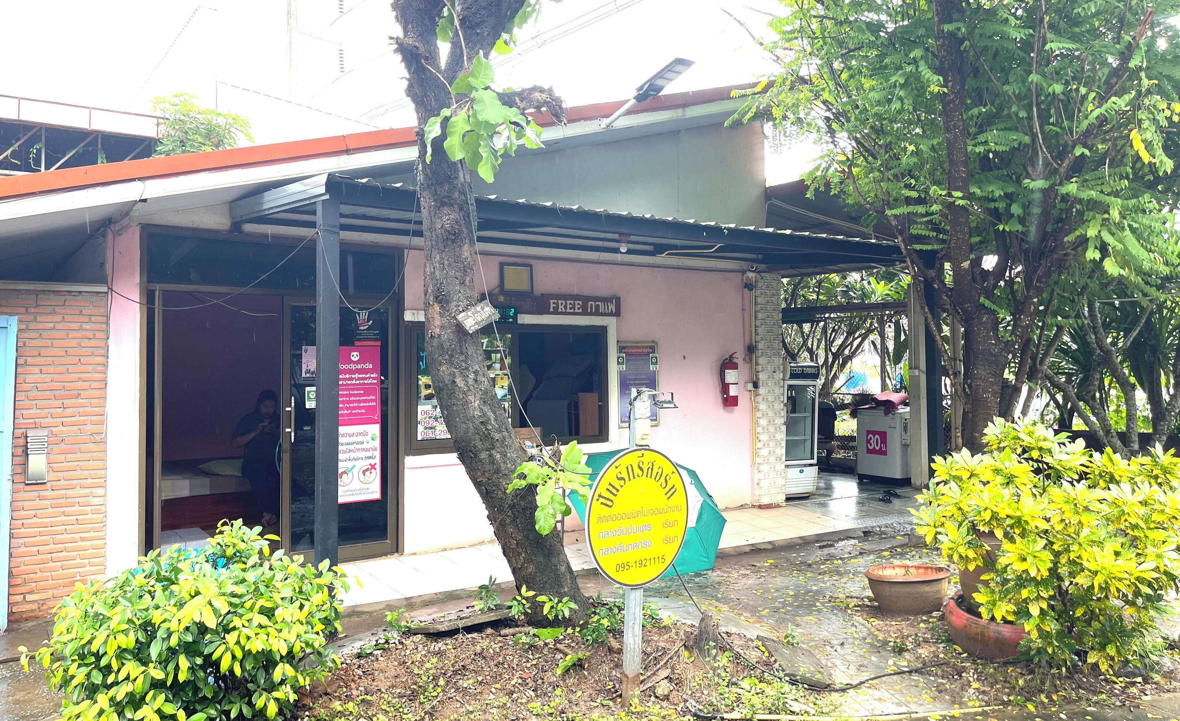 A small building with a signboard, a water dispenser, and a tree in front.