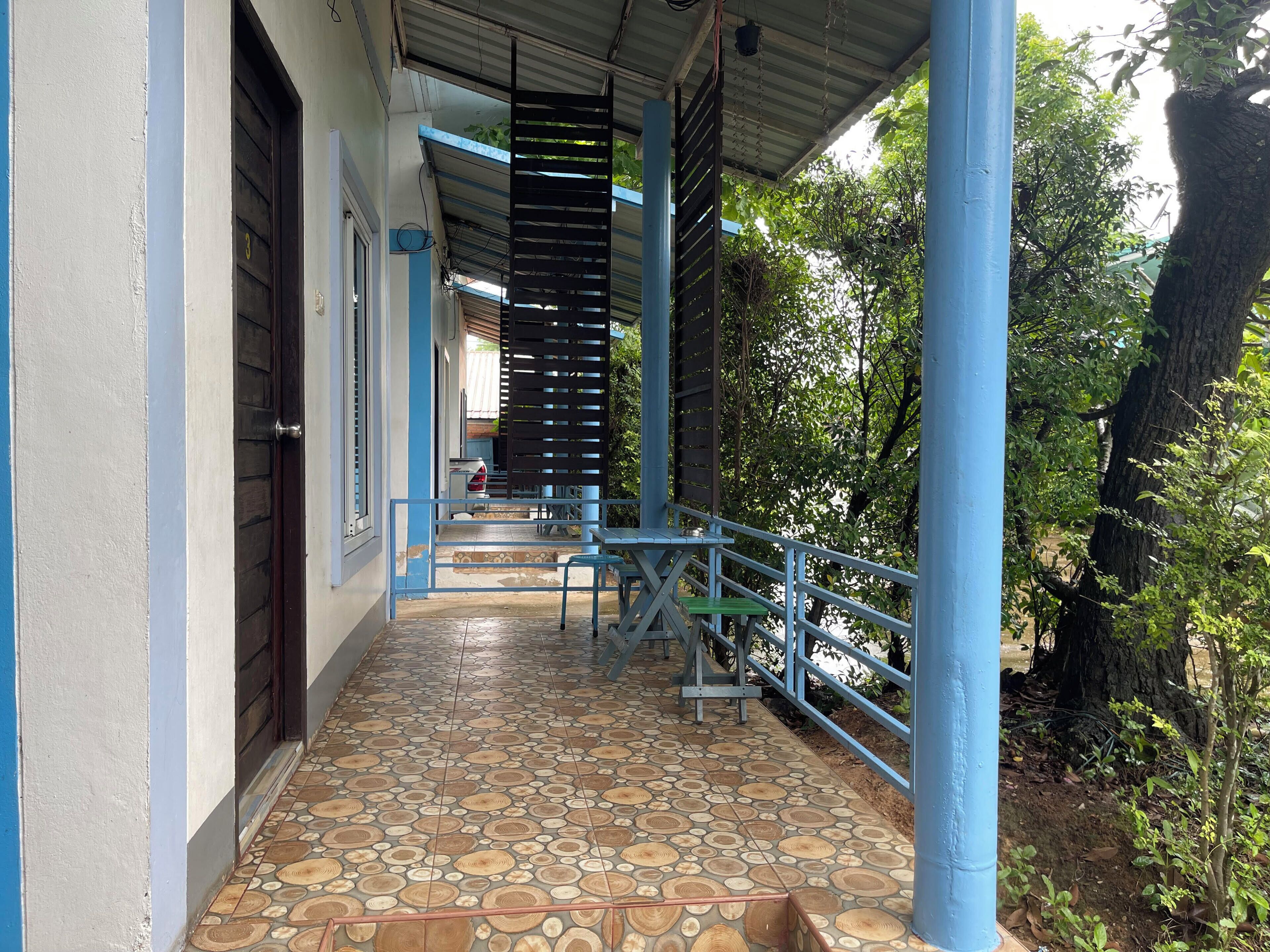 A covered outdoor area with a tiled floor, blue railings, and a staircase leading to a higher level.