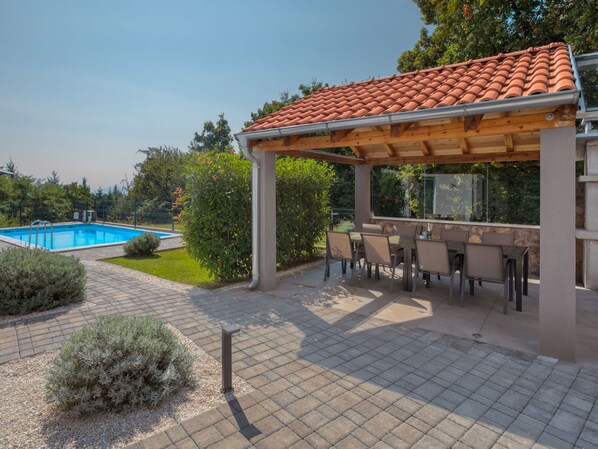 A covered outdoor area with a pool, patio furniture, and a pergola with a tiled roof.