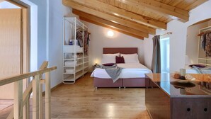 A bedroom with a wooden ceiling, a bed with white bedding, a bedside table, and a wardrobe with hanging clothes.