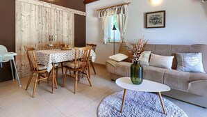 A dining area with a wooden table and chairs, a sofa, and a small round table with a vase.