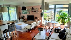 Ein modernes Wohnzimmer mit Sofa, Sesseln, Esstisch und Fernseher.