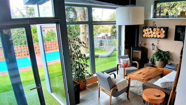 Ein modernes Wohnzimmer mit großen Glasschränken, die zum Garten führen, einem Kamin und einem Essbereich.