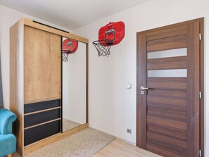 A room with a wooden wardrobe, a basketball hoop, a door with a peephole, and a blue chair.