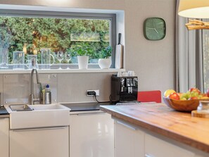 A kitchen with a window, a sink, a coffee machine, and a bowl of fruit on the counter.
